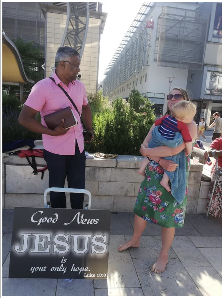 A street preacher holding an open Bible beside a sign