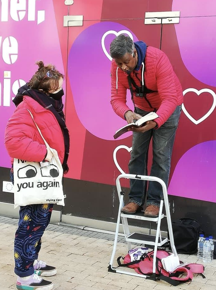 A man speaking from a stepladder to a passer-by