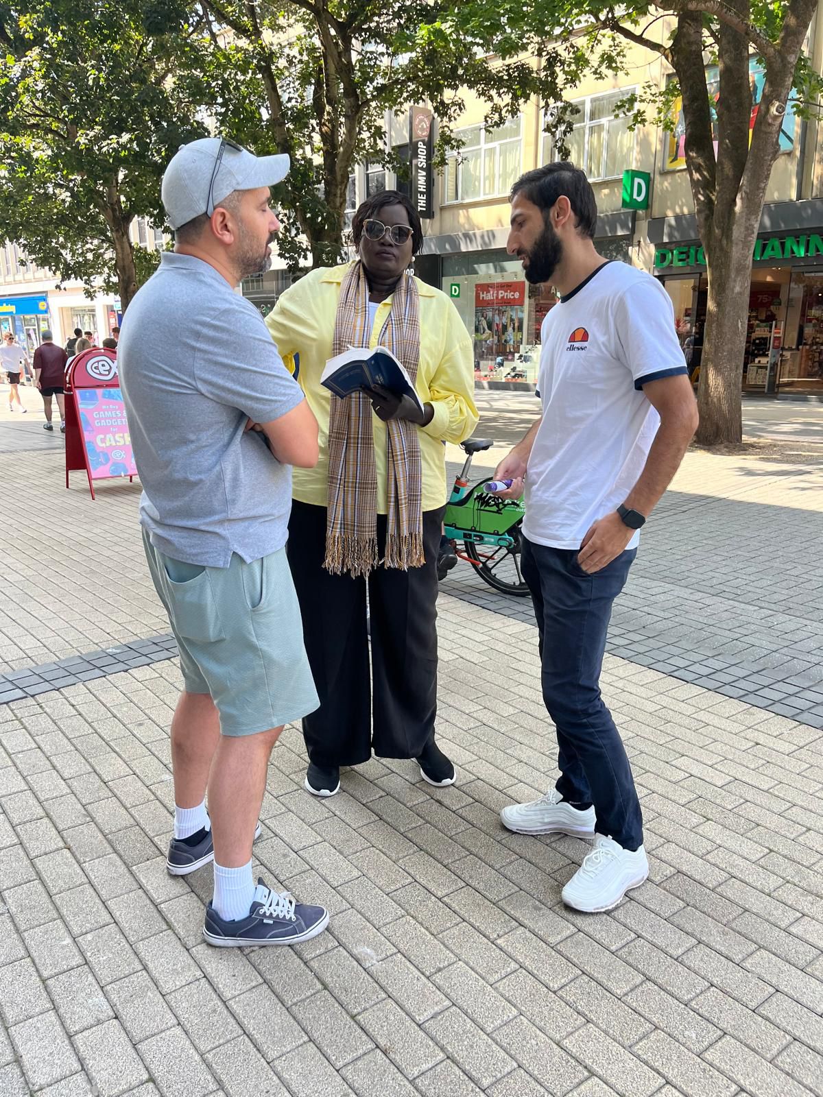 A woman showing a book to two men outdoors