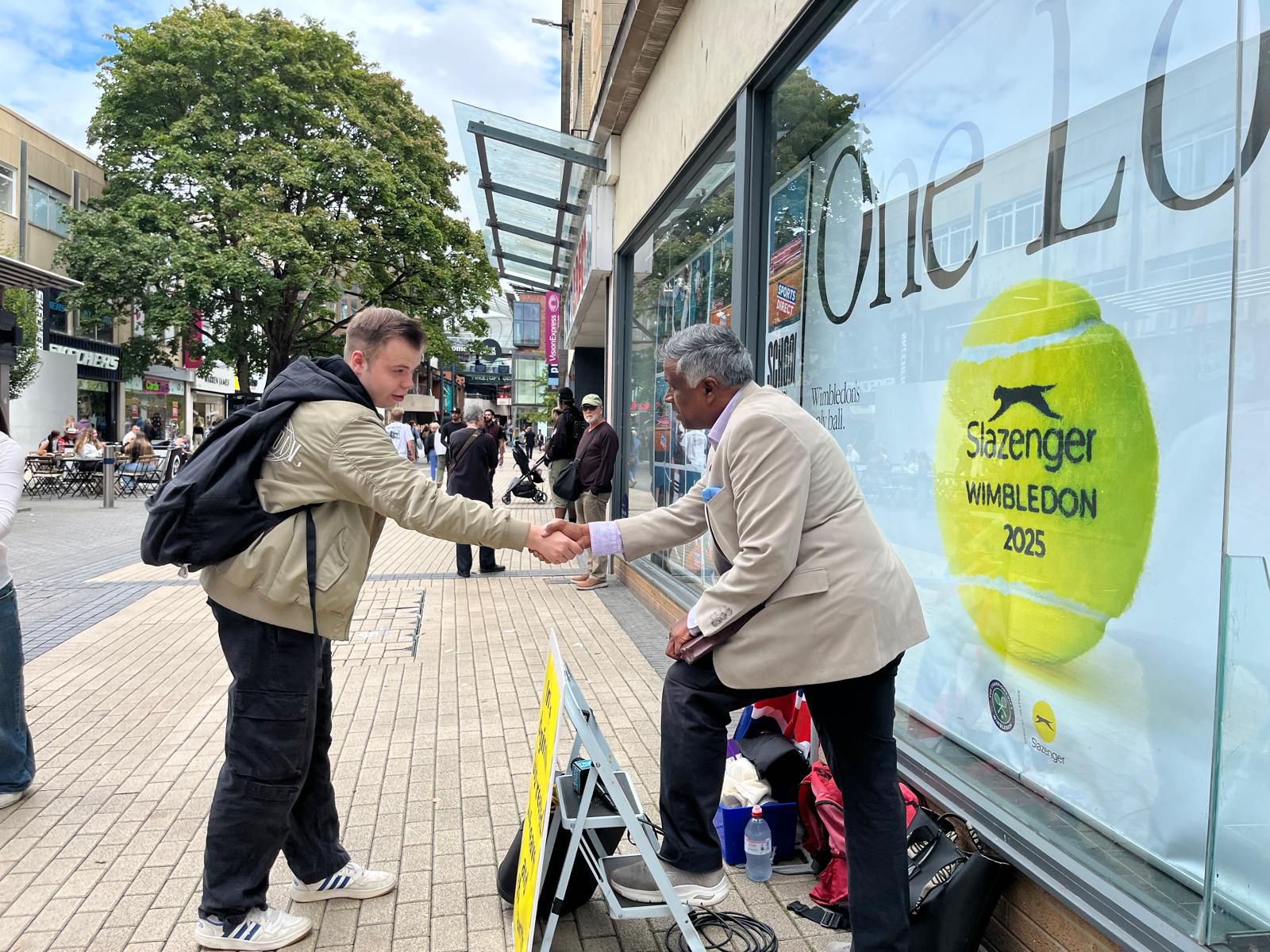 A man on a stepladder shaking hands with a passer-by